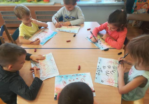 Grupa dzieci zainspirowana obrazem „Odlot żurawi” Chełmońskiego rysuje przy stoliku odlatujące ptaki.